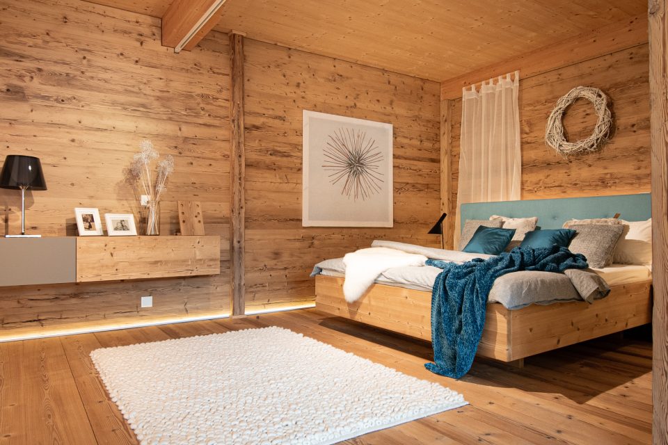 Schlafzimmer nach Innenausbau und Umbau mit Holzboden Wände mit Holz verkleidet Sideboard schweben und einem Bettgestell mit Polsterkopfteil und Hüsler Nest Bettinhalt