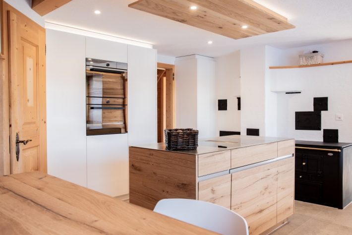 Umbau Innenausbau von Wohnhaus mit Blick in die Küche mit Kochinsel aus Eiche Altholz grauen Bodenplatten und weisse Küchenfronten